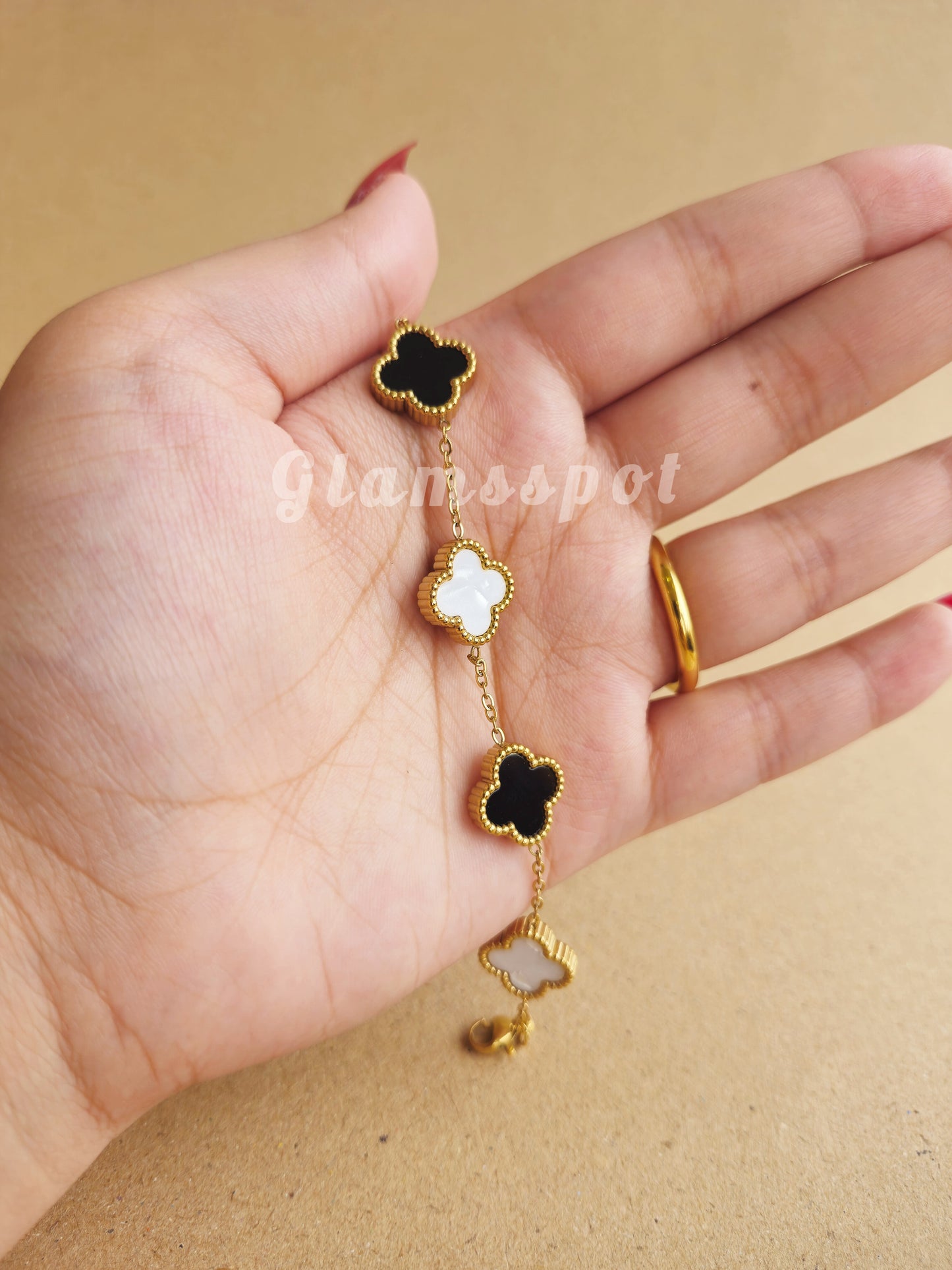 Gold and black clover-shaped Bracelet held in a hand against a beige background.