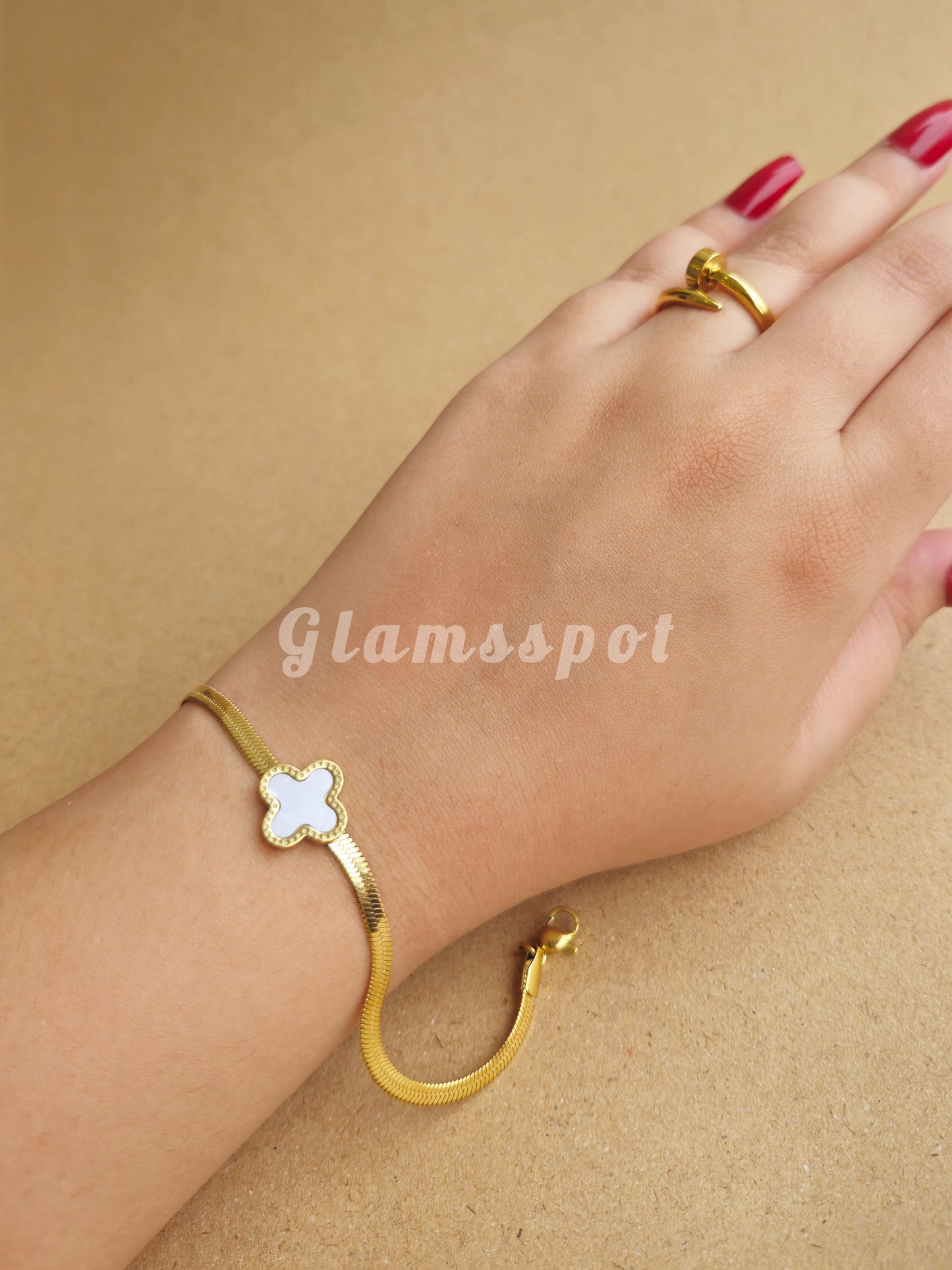 Gold bracelet and ring on a hand against a beige background with 'Glamsspot' branding.