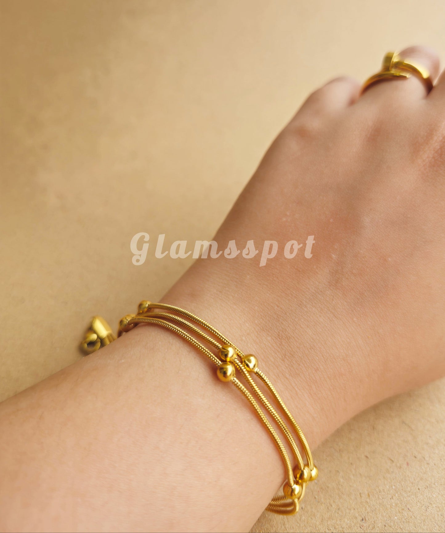 Gold bracelet on a wrist with a beige background