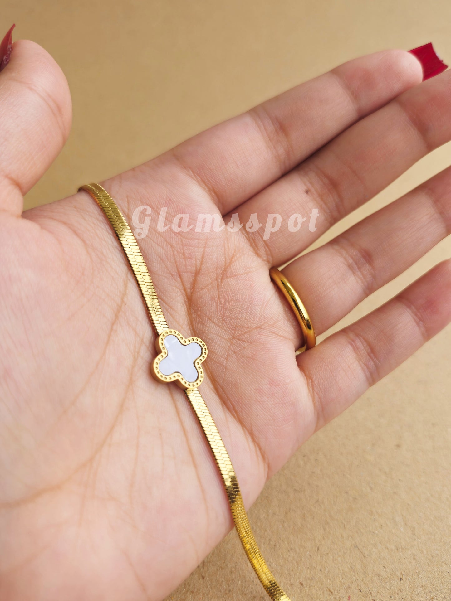 Gold bracelet with a white Flower Vancleef charm on a hand against a beige background