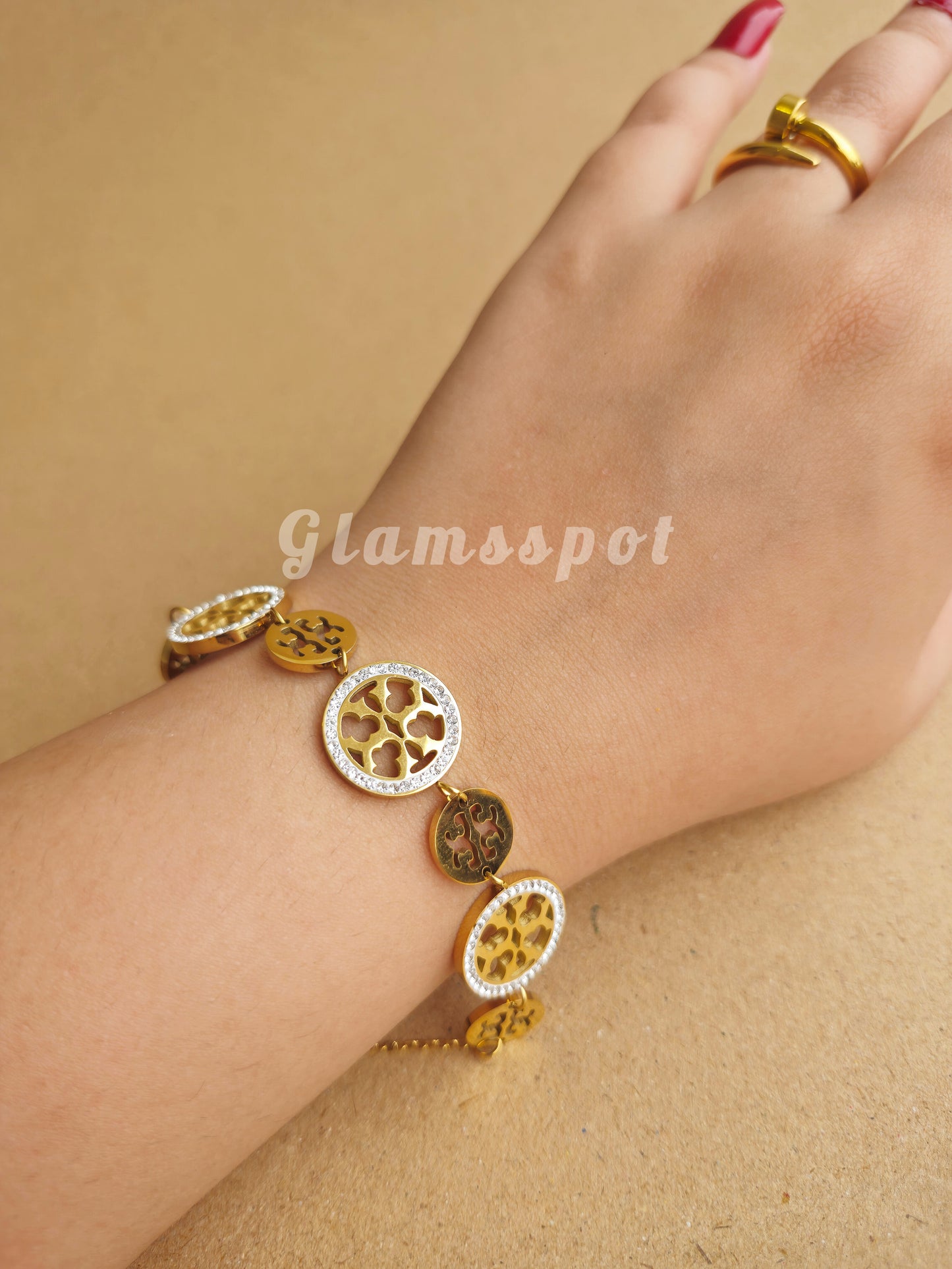 Gold Tory Burch Bracelet with circular charms on a wrist against a beige background, featuring the brand 'Glamspot'.