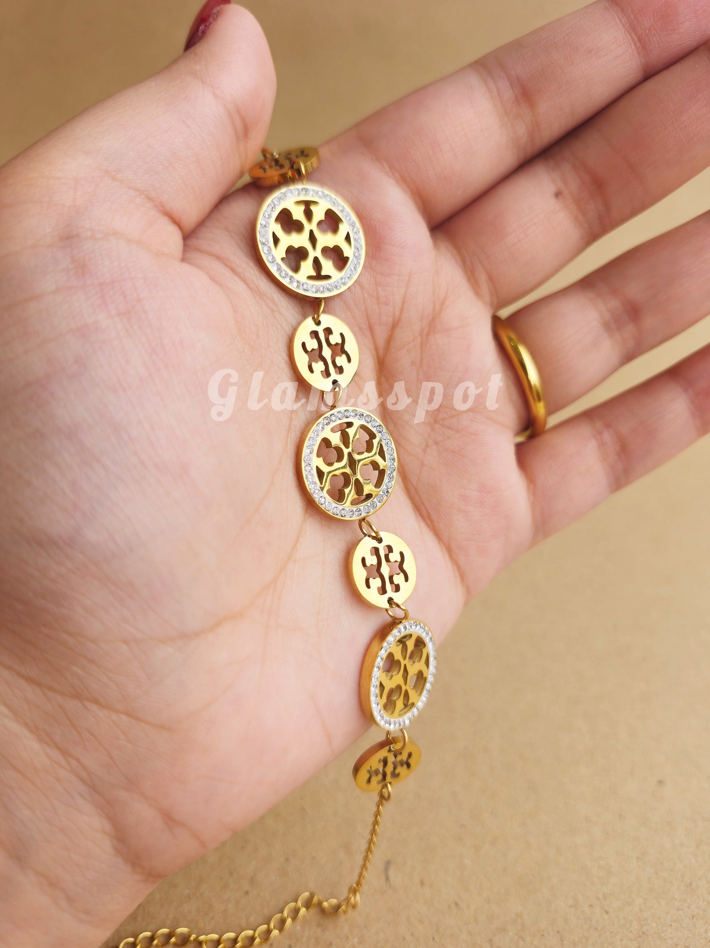 Gold Tory Burch Bracelet with decorative elements on a hand against a beige background