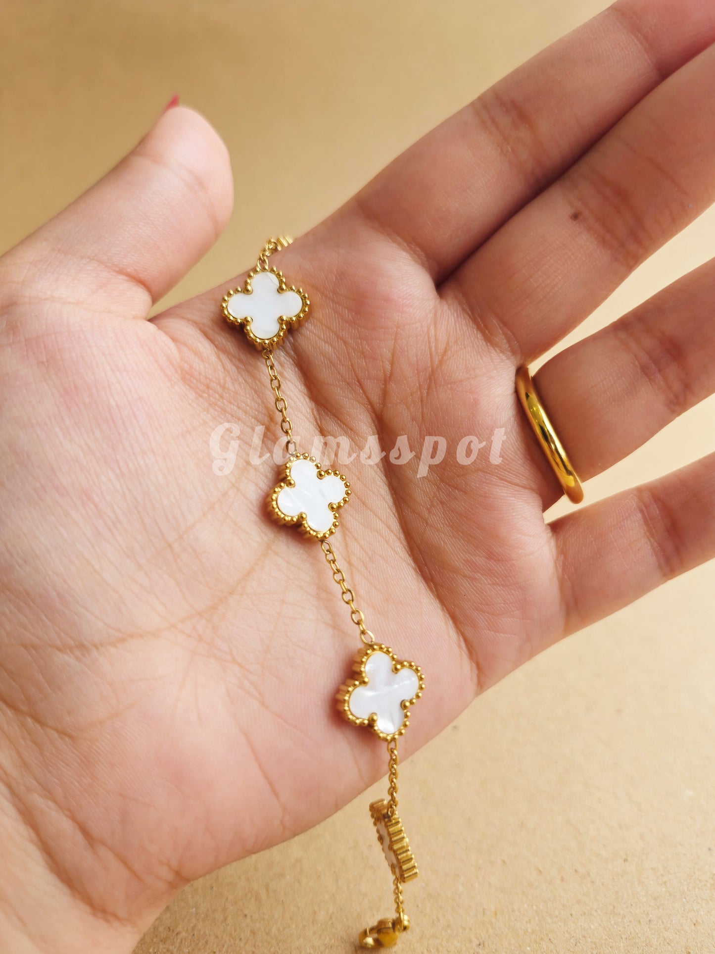 Gold and white clover-shaped bracelet on a hand against a beige background