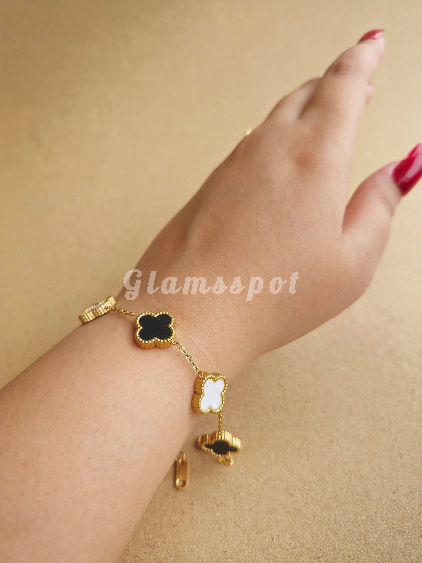 Gold bracelet with clover charms on a wrist against a beige background, branded 'Glamsspot'.