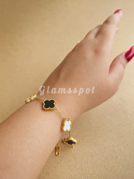 Gold bracelet with clover charms on a wrist against a beige background, branded 'Glamsspot'.