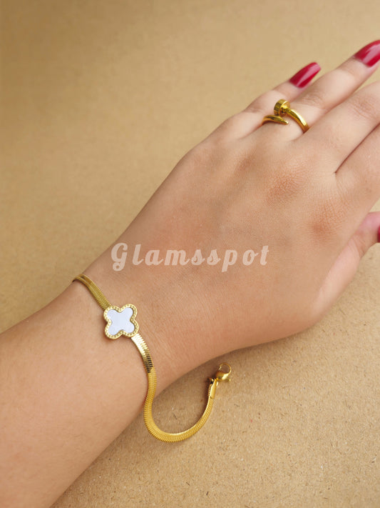 Gold bracelet and ring on a hand against a beige background with 'Glamsspot' branding.