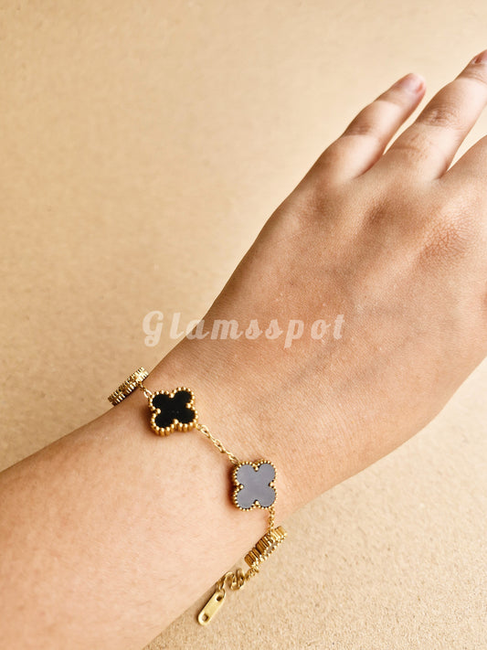 Black Clover Bracelet with clover-shaped charms on a wrist against a beige background, branded 'Glamspot'.