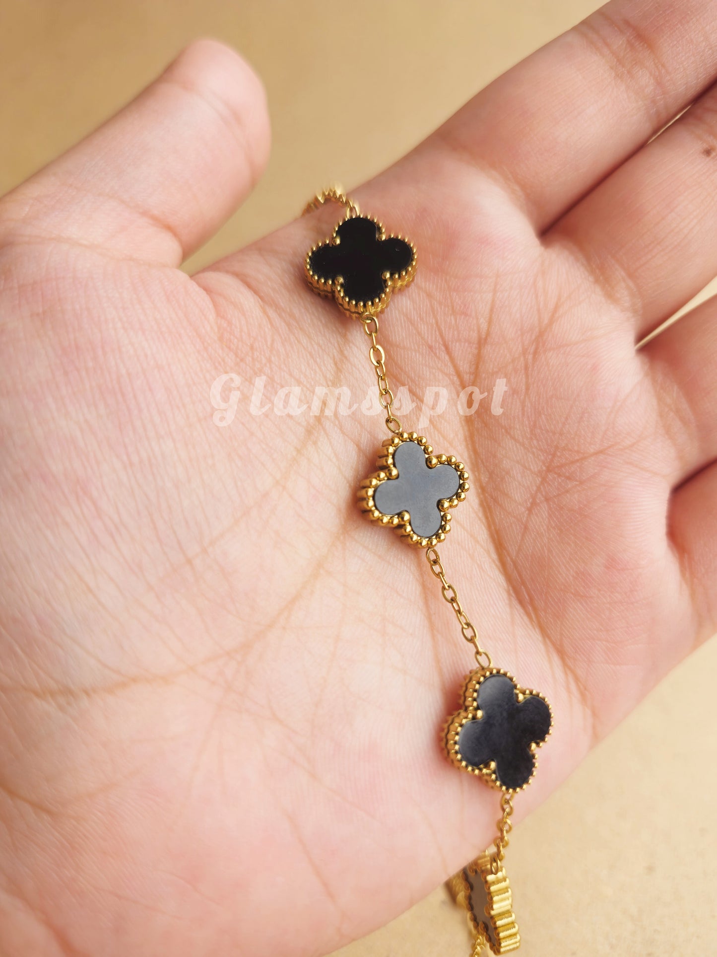 Gold and black clover-shaped Bracelet held in a hand against a beige background.