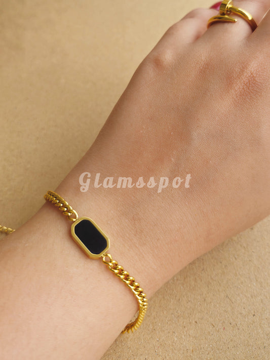 Gold Black Dial Bracelet with a black stone on a wrist against a beige background, branded 'Glamsspot'.