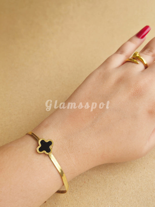 Black Vancleef Bracelet with clover design on a wrist against a beige background, branded 'Glamsspot'.