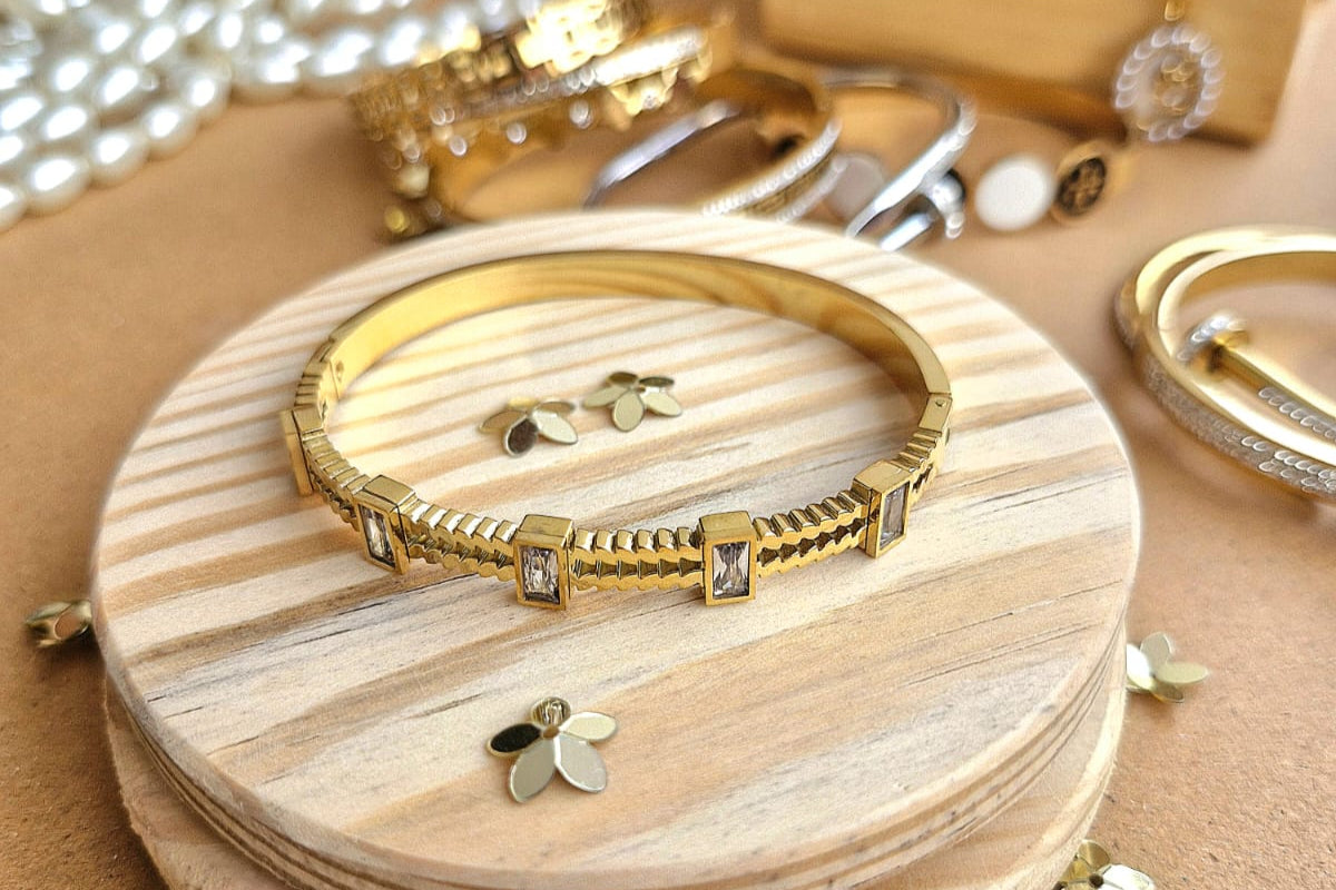 Chunky-Rhinestone Gold bracelet on a wooden stand with other jewelry items on a beige background