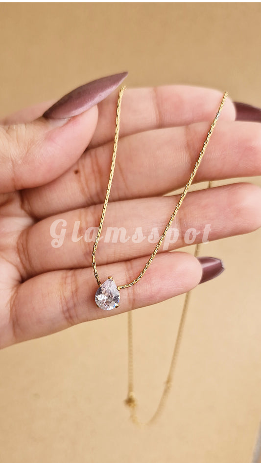 Gold necklace with a heart-shaped pendant held by a hand on a beige background