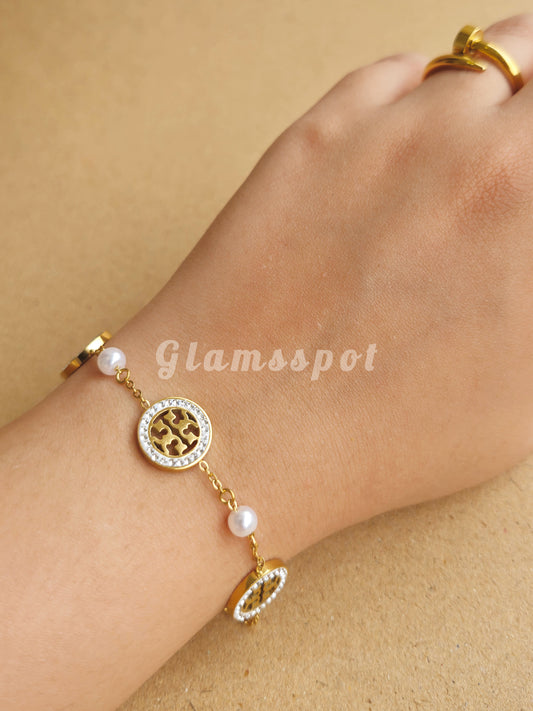 Gold Minimal Tory Bracelet with circular design and pearl-like beads on a wrist against a beige background, branded 'Glamsspot'.