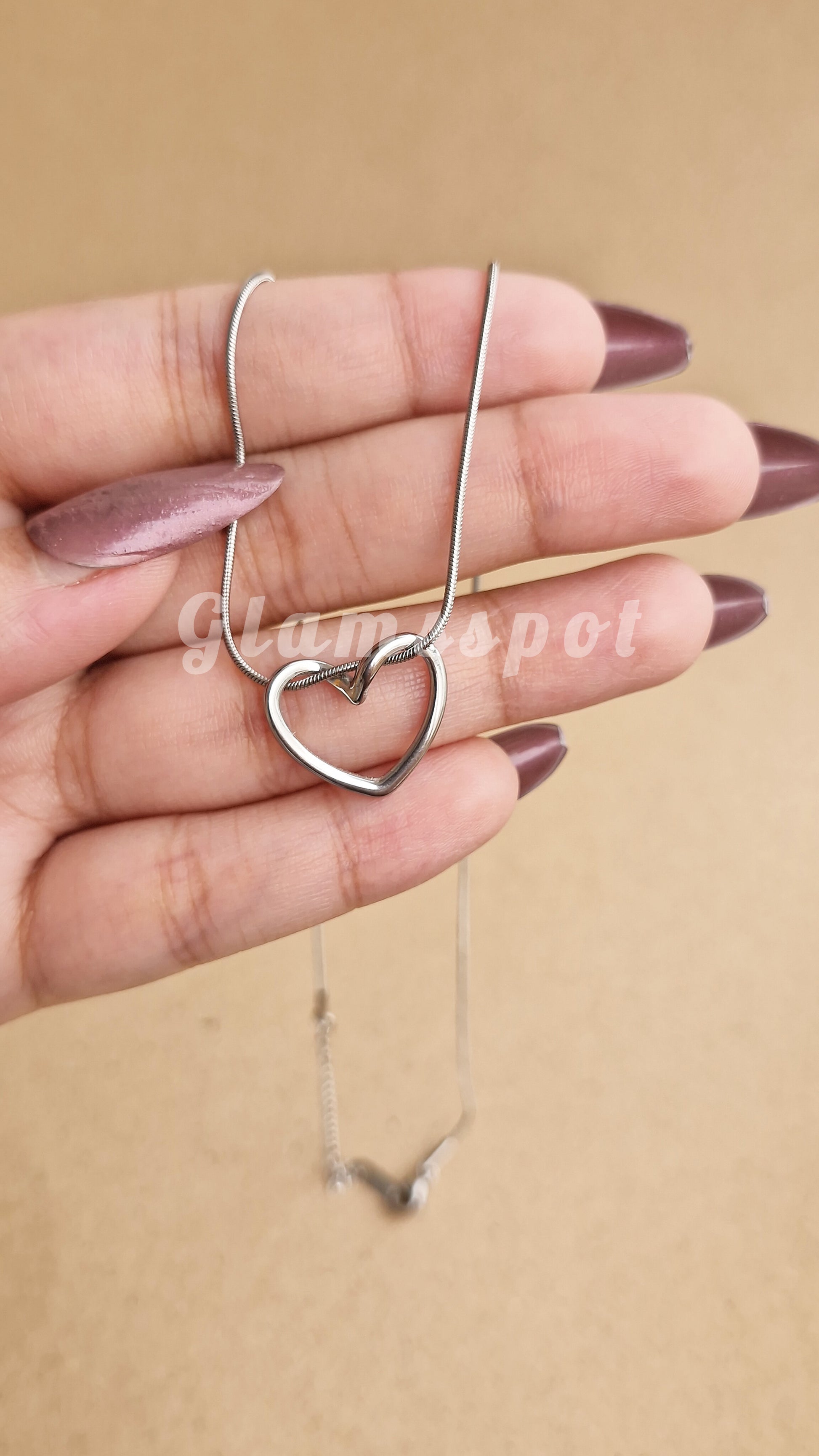 Heart-shaped necklace held by a hand with a beige background