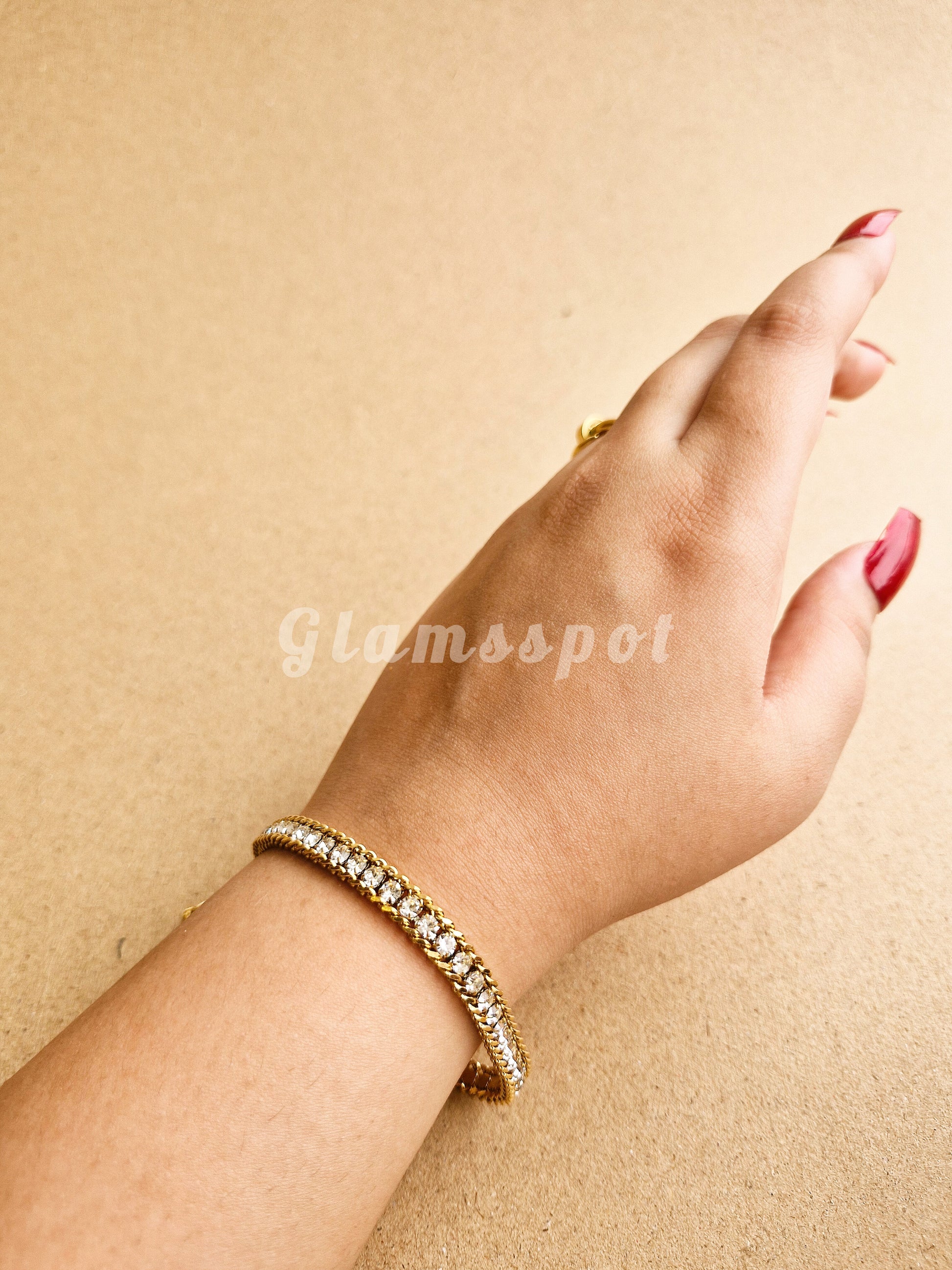 Hand wearing a gold Tennis Bracelet on a beige background with 'Glamsspot' branding.