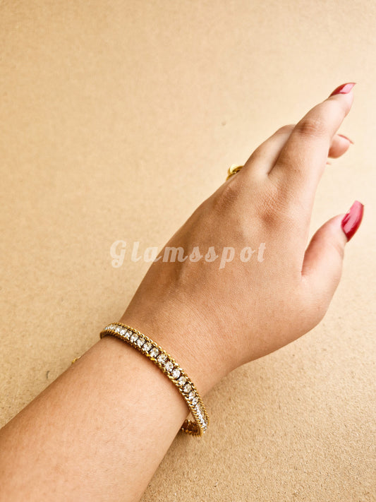 Hand wearing a gold Tennis Bracelet on a beige background with 'Glamsspot' branding.