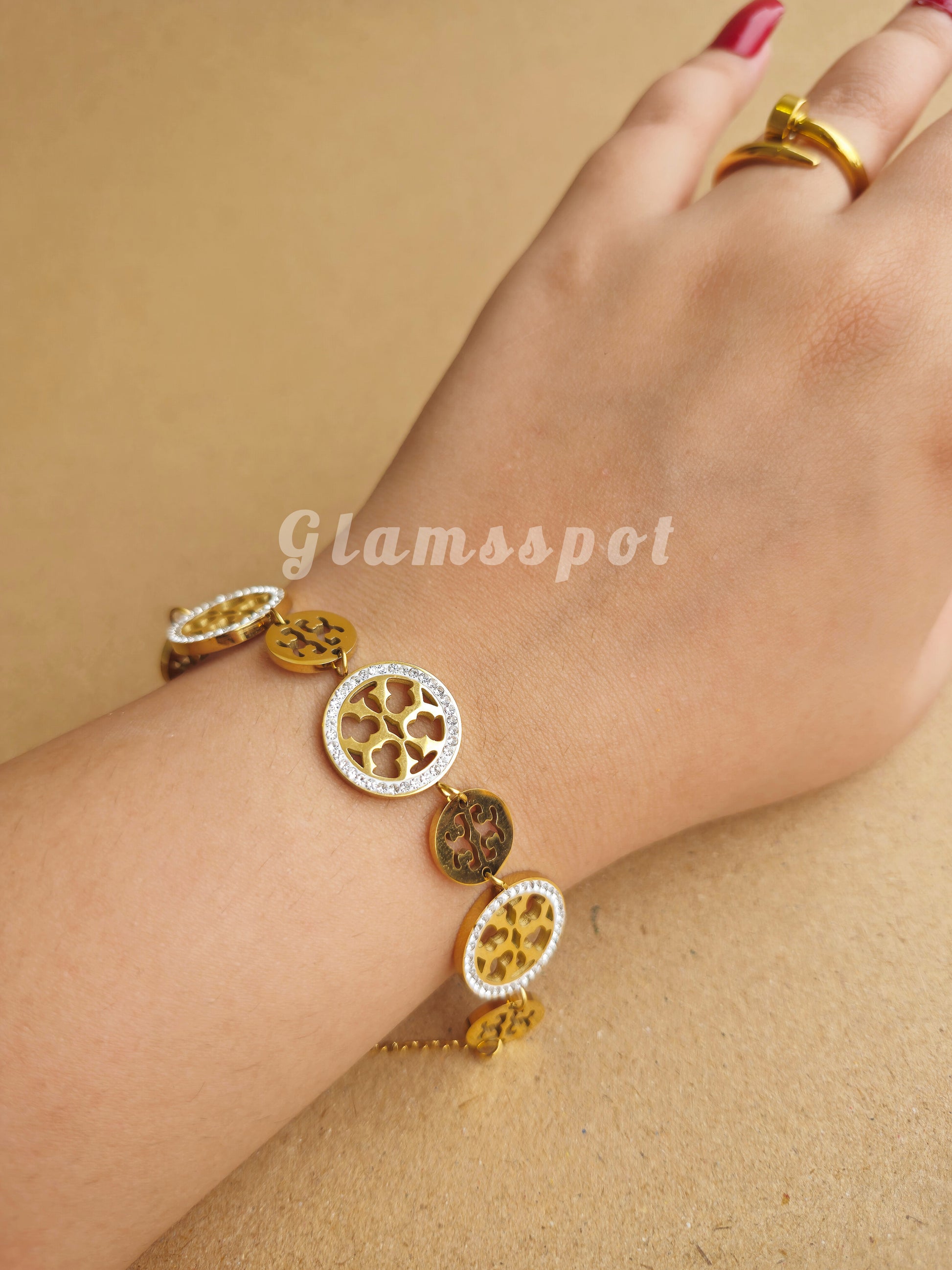 Gold Tory Burch Bracelet with circular charms on a wrist against a beige background, featuring the brand 'Glamspot'.