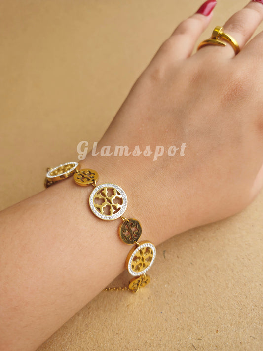 Gold Tory Burch Bracelet with circular charms on a wrist against a beige background, featuring the brand 'Glamspot'.