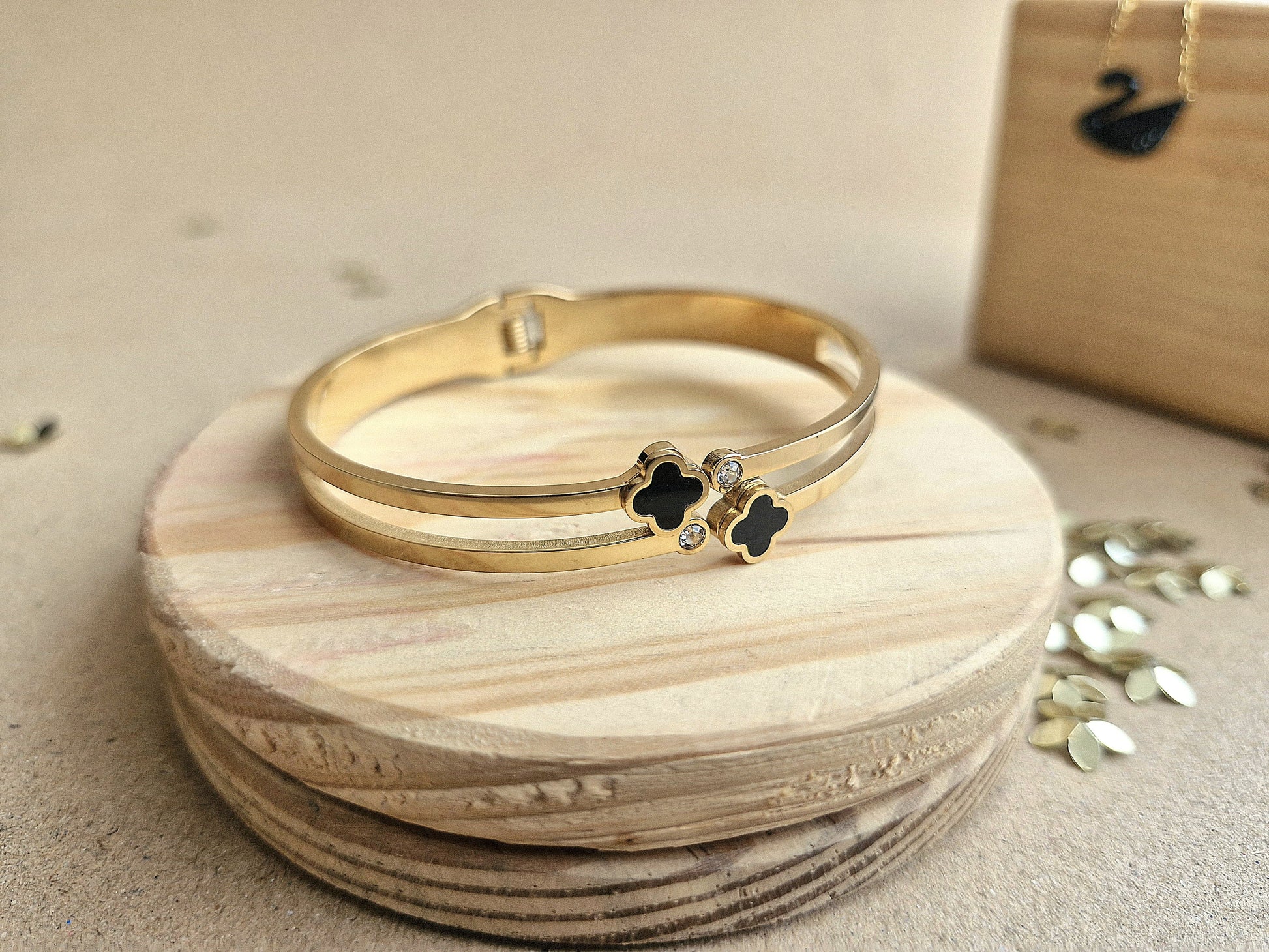 Gold bracelet with black clover charms on a wooden surface