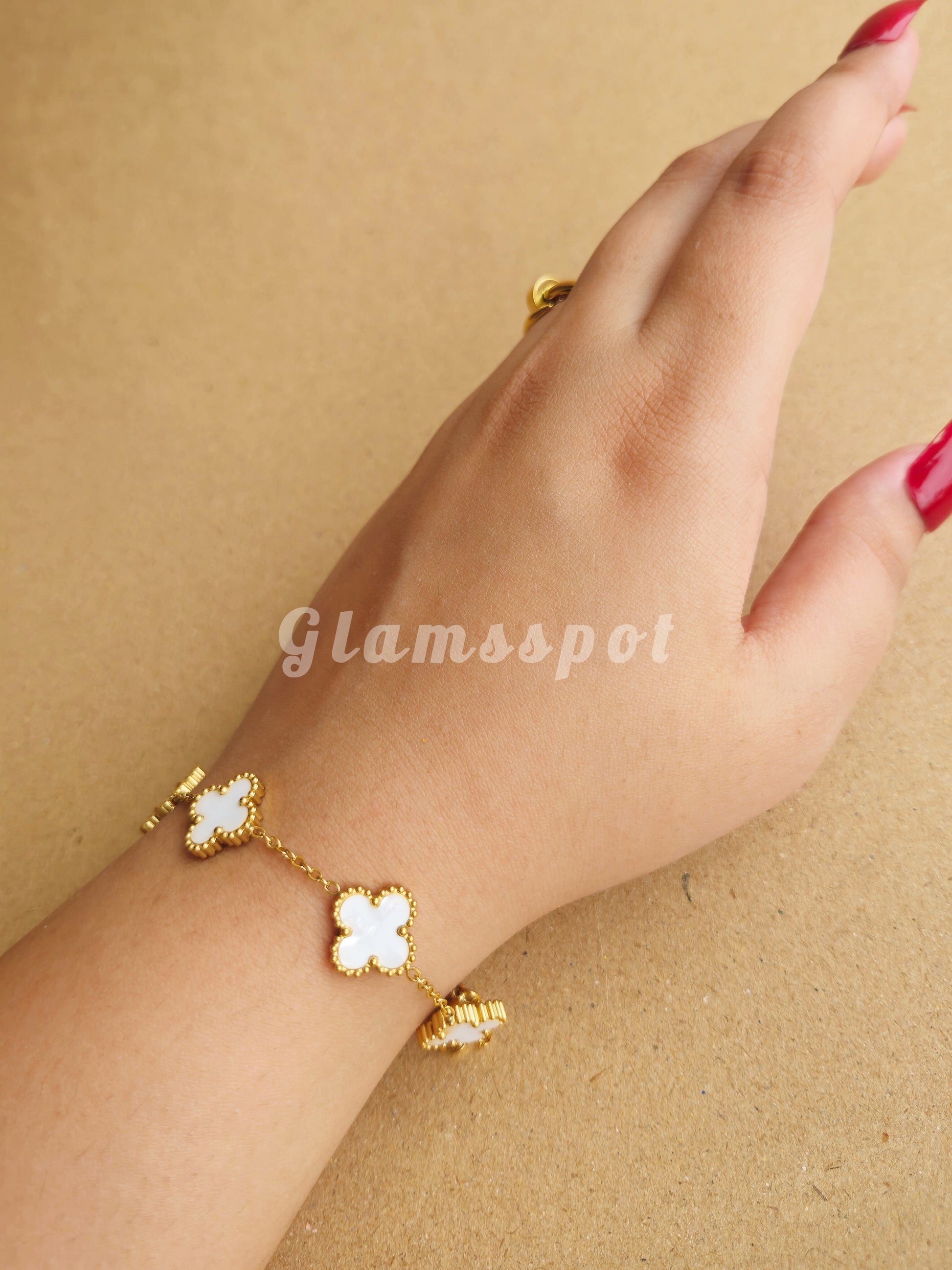 White Clover Bracelet with clover-shaped charms on a wrist against a beige background, branded 'Glamsspot'.